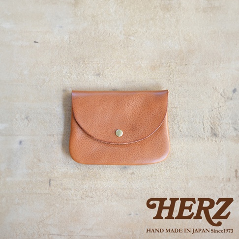 棕色皮革製成、帶有鈕扣的橢圓形小物收納袋，置於淺色木紋背景上。