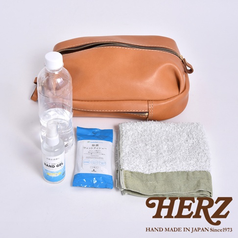 一個皮革側背包，旁邊有一個水瓶、一包濕紙巾和一條毛巾。