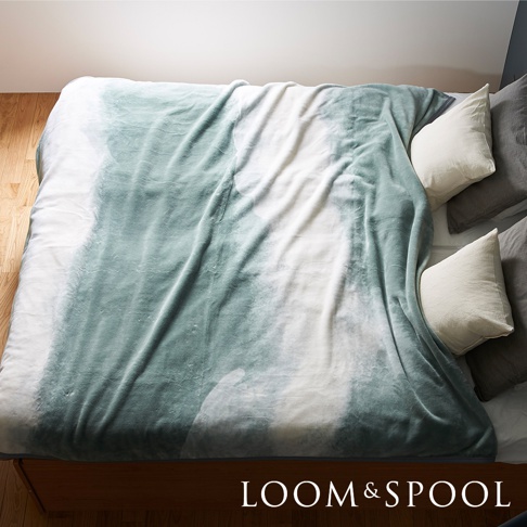 一張鋪在雙人床上的淺綠色與白色漸層印花短絨毯，質地柔軟，毯子上有明顯的絨毛紋理。