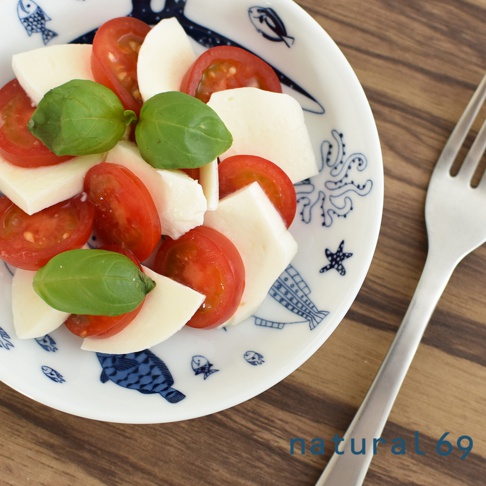 白色陶瓷小碟，飾有藍色海洋生物圖案，盤中盛有切片番茄、莫札瑞拉起司塊和羅勒葉，組成卡布里沙拉。