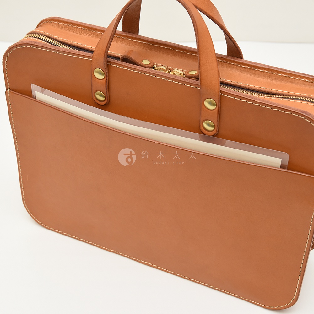 棕色皮革製成的手提公事包，設有拉鍊主隔層和外部插袋，搭配皮革提把和金色金屬配件，展現職人手作質感。