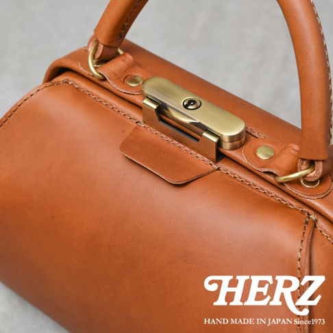 職人手作咖啡色皮革兩用口金手提包，帶有黃銅色金屬鎖扣和提把，皮革表面有自然紋理。