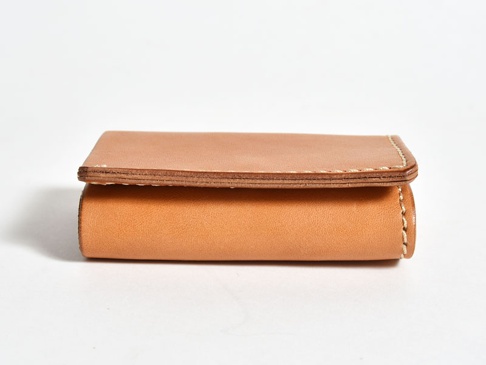 淺棕色皮革三折式迷你短夾，簡潔設計，邊緣有縫線細節，材質為真皮，小巧便攜。