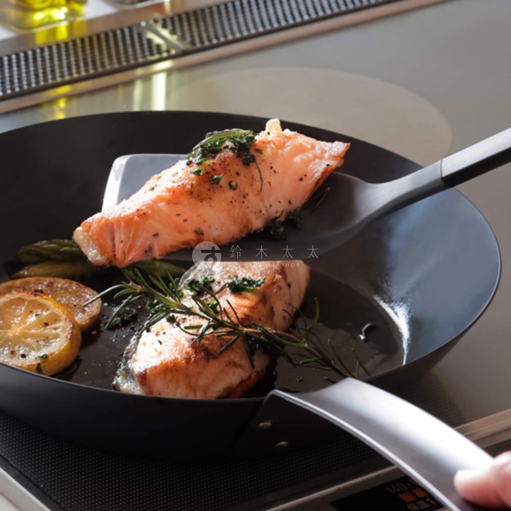 煎鍋中烹調好的香煎鮭魚，旁邊擺放著檸檬片和迷迭香，一旁有著專用的黑色料理煎鏟，上面印有日文的鈴木太太標誌