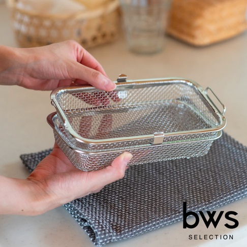 一雙手正拿著一個銀色不鏽鋼網狀洗碗機專用清潔收納盒，其表面有細密的網格和兩個金屬卡扣。