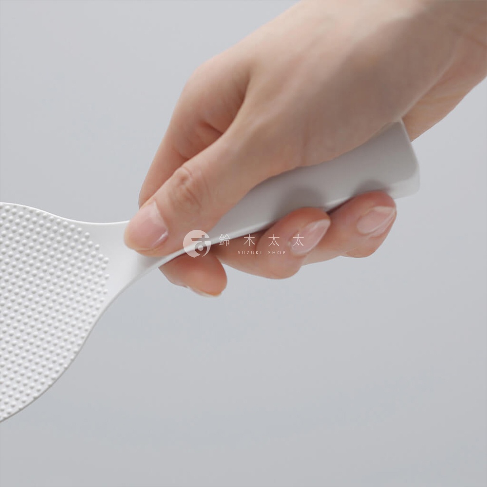 手握白色站立式飯匙，飯匙上有細小的顆粒壓紋，背景為淺灰色。