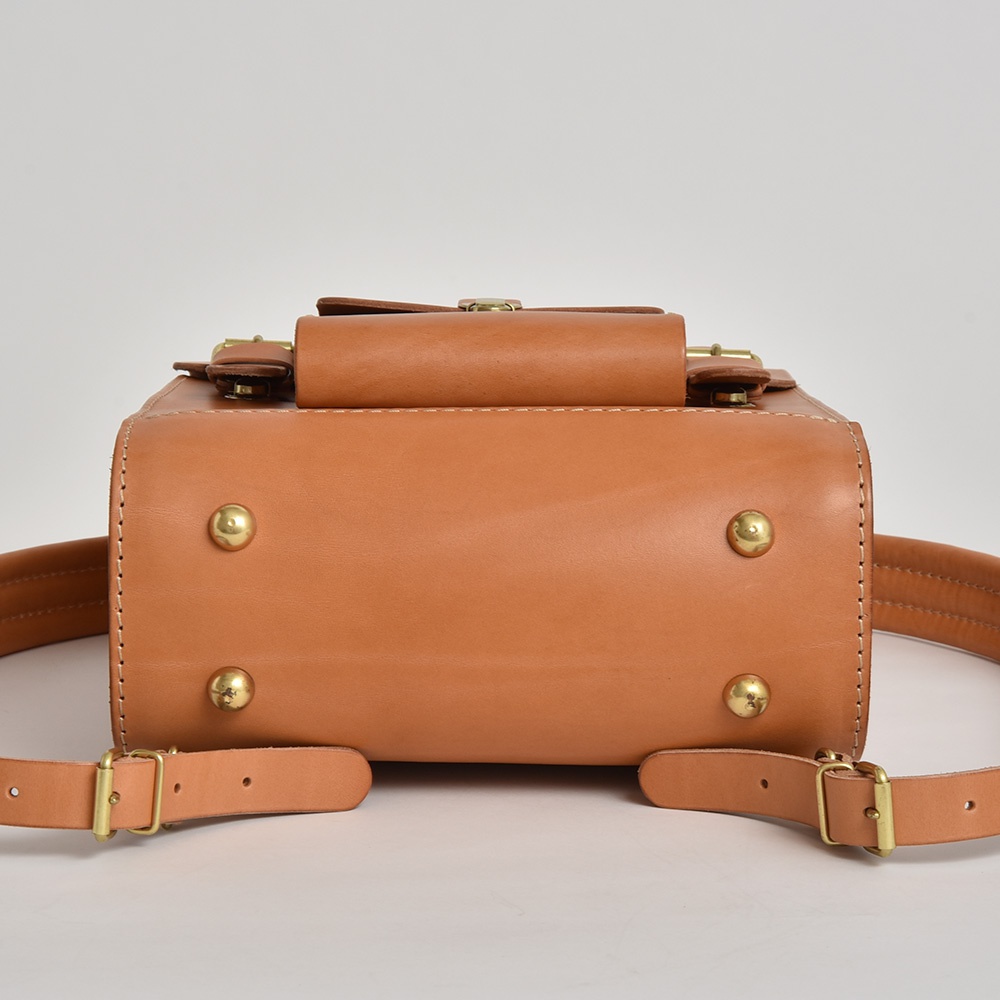 職人手作皮革經典學院風後背包 R-100，採用原色牛皮材質，配有黃銅扣環及鉚釘，展現復古質感。