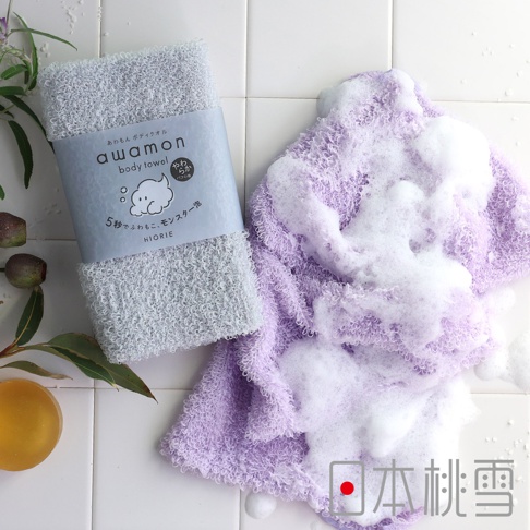一條淺灰色、包裝著的awamon沐浴巾，旁邊是一條淺紫色、帶豐富泡沫的沐浴巾。兩條沐浴巾皆為網狀織紋。