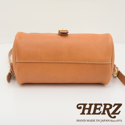 職人手作皮革屋瓦風後背包，淺棕色牛皮材質，圓筒狀設計，頂部有皮質束繩和金屬釦環，側邊有皮革揹帶。