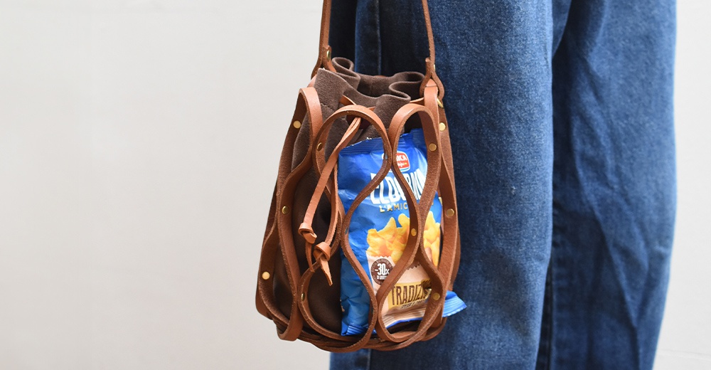 一個裝有零食的皮革水桶包，由藍色牛仔褲襯托