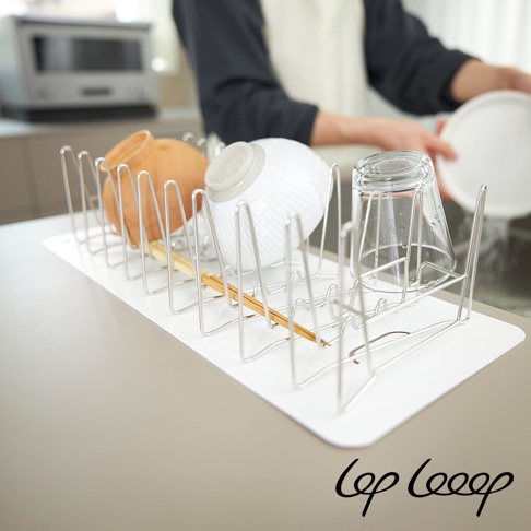 銀色不鏽鋼伸縮式瀝水架，架上擺放著一個橘色陶碗、一個白色條紋碗和一個透明玻璃杯，下方鋪有白色防水墊，背景為廚房場景。
