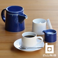 藍色M型壺，白色咖啡杯與盤子，白色糖罐，藍色奶盅，以及銀色湯匙，皆為陶瓷材質，置於木質桌面。