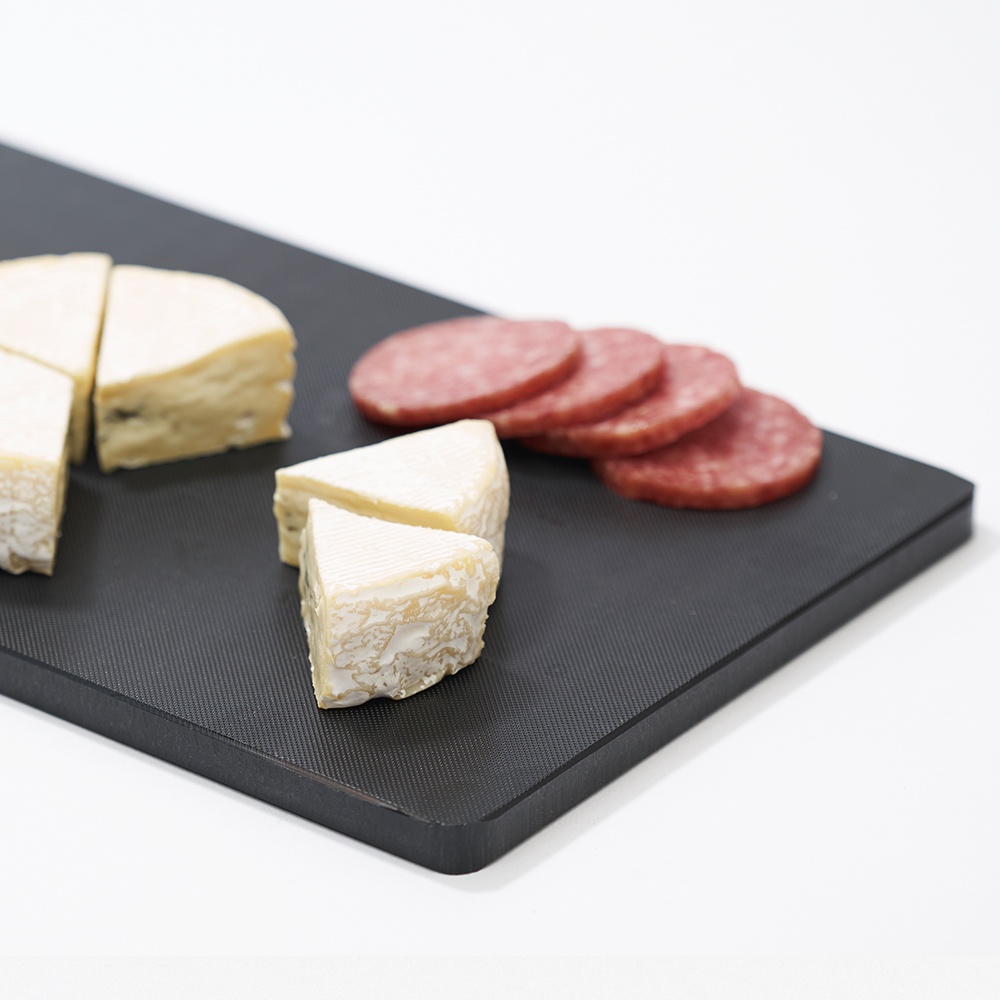 黑色紋理砧板，上面擺放著切塊的起司和數片香腸。