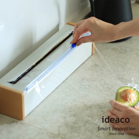 日本製原木鋼製保鮮膜切割器，白色機身搭配木質邊框，內嵌鋼製刀片，藍色滑塊用於切割保鮮膜。