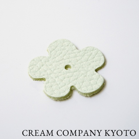 淺綠色皮革製成、五瓣花朵造型的飾品，帶有細緻皮革紋理，中央有一個小圓孔。