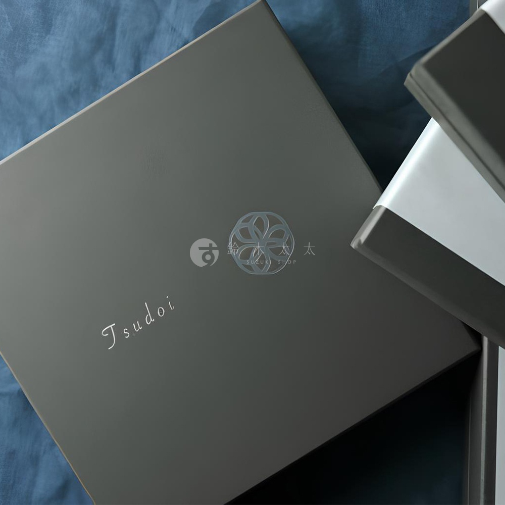 Tsudoi 品牌名稱壓印在深灰色禮盒上，禮盒中央有銀色圓形花紋和日文 logo。另一個禮盒的側面露出，為淺白色與深灰色條紋設計。