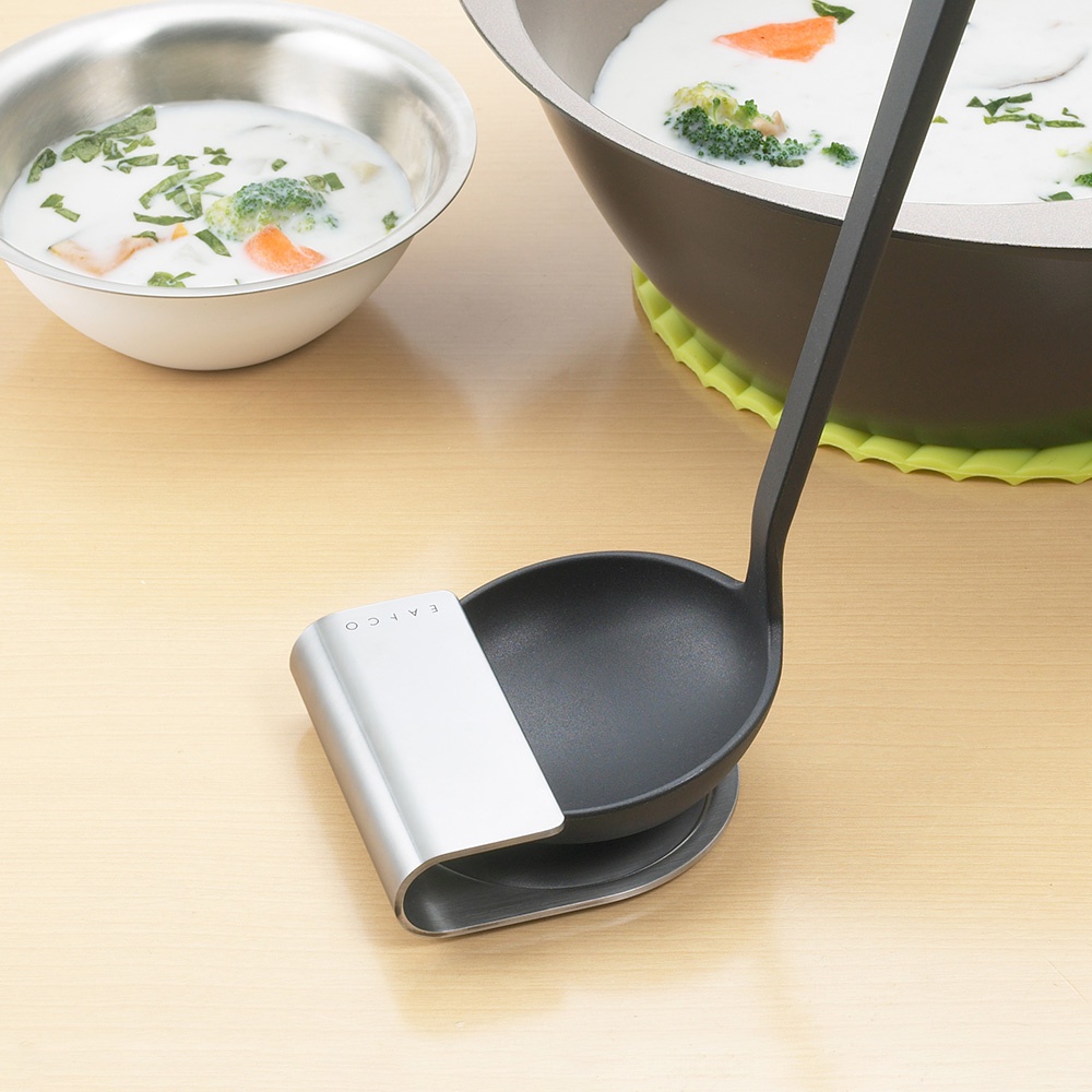 一個銀色金屬湯杓座，搭配一個黑色湯杓，湯杓內盛有白色濃湯及蔬菜塊，湯杓座上刻有「EAPCO」字樣。