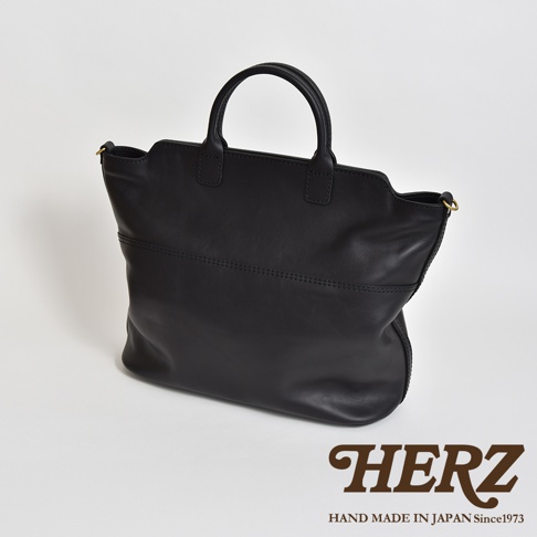 黑色皮革手作托特包，具有簡潔的設計和兩條提把。包身前方有兩條橫向縫線裝飾，整體呈現自然垂墜感。