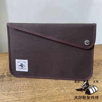 深棕色純棉帆布平板收納包，配有斜織帶裝飾和按鈕開合。左側有一個印有日文圖標的白色標籤。