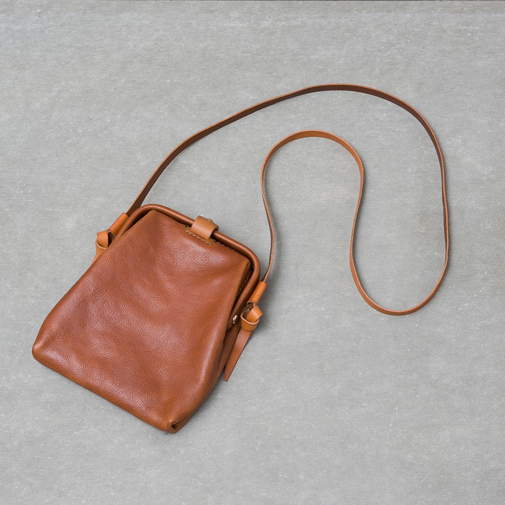 職人手作的咖啡色皮革迷你杜勒斯側背包，附有細長可調節的皮革背帶，包身呈現柔軟的皺褶感，並飾有皮革繫帶細節。