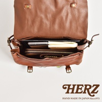 職人手作皮革復古郵差包，棕色皮革，內部裝有筆記本、手機和皮夾，展現自然紋理與復古風格。