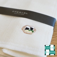 白色網格狀的八重紗擦拭巾，繡有兩個日式飯糰圖案，搭配深色品牌束帶。