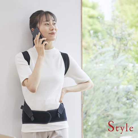 一名女性身穿白色短袖上衣，佩戴著黑色BX Pro美姿調整背帶。背帶由彈性布料製成，具有可調節的肩帶和腰部固定帶，有效支撐背部。