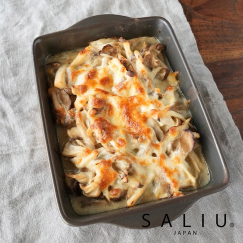 裝盛在 Saliu 日本品牌深褐色長方形耐熱陶盤中的焗烤料理，盤內鋪滿新鮮蕈菇並覆蓋著烤至焦香金黃的融化起司，呈現出誘人的溫暖餐桌氛圍。