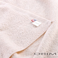 米白色的今治沙龍毛巾，質地柔軟，絨毛蓬鬆，毛巾上帶有品牌標籤，標籤上印有「ORIM」字樣及網址，並有紅藍色塊裝飾。