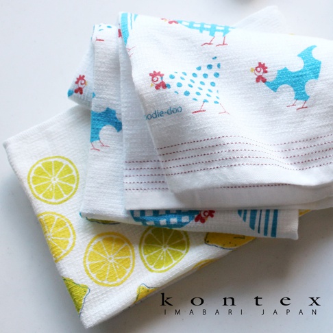 白色毛巾堆疊，其中一條印有黃色檸檬片圖案，另一條印有藍色和紅色小雞圖案，材質輕薄透氣，觸感柔軟。