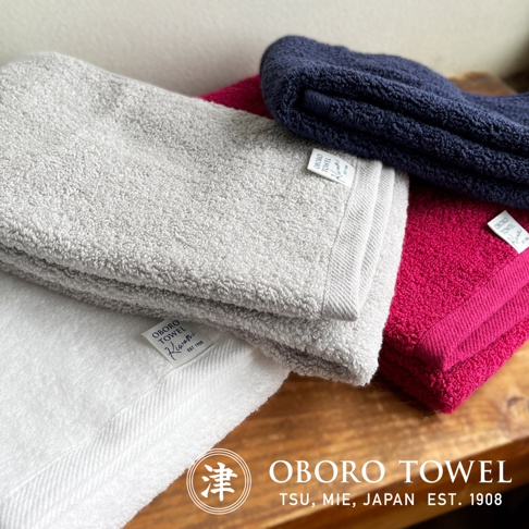 堆疊的毛巾，顏色為白色、淺灰色、桃紅色和海軍藍，材質為竹棉，織紋細膩，邊緣有品牌標籤。