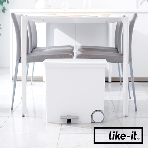 白色寬型腳踏式分類垃圾桶，配有灰色腳踏板和兩個輪子，置於餐桌下方，旁邊有幾張灰色椅子。