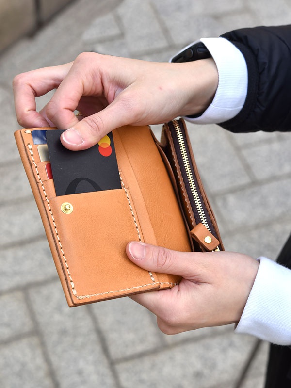 職人手作皮革中型雙折短夾，淺棕色皮革，內有卡片槽與拉鍊零錢袋，以手工縫線和金色卯釘裝飾。