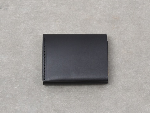 黑色皮革雙折迷你短夾，特寫展示其簡潔設計與縫線細節，材質光滑，風格俐落。