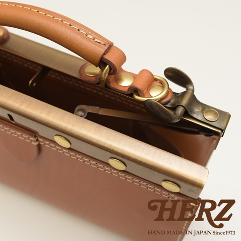 職人手作皮革復古口金兩用手提包，採用淺棕色皮革，搭配古銅色金屬口金和提把，展現經典復古風格。包包邊緣有精緻的縫線細節，金屬配件質感良好。