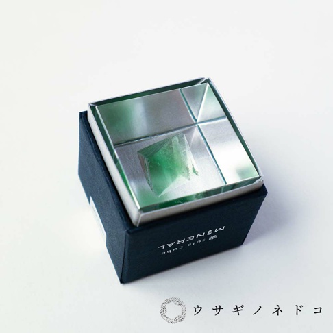 Sola cube 礦石立方塊，內含一塊綠色螢石，置於銀色金屬盒內，盒蓋為鏡面設計，映照出礦石的晶瑩剔透。