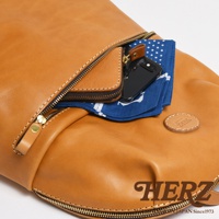 職人手作皮革後背包，棕褐色，圓角大開口設計，前袋露出手機、藍色印花手帕及零錢包，金色拉鍊，圓形皮革標誌。