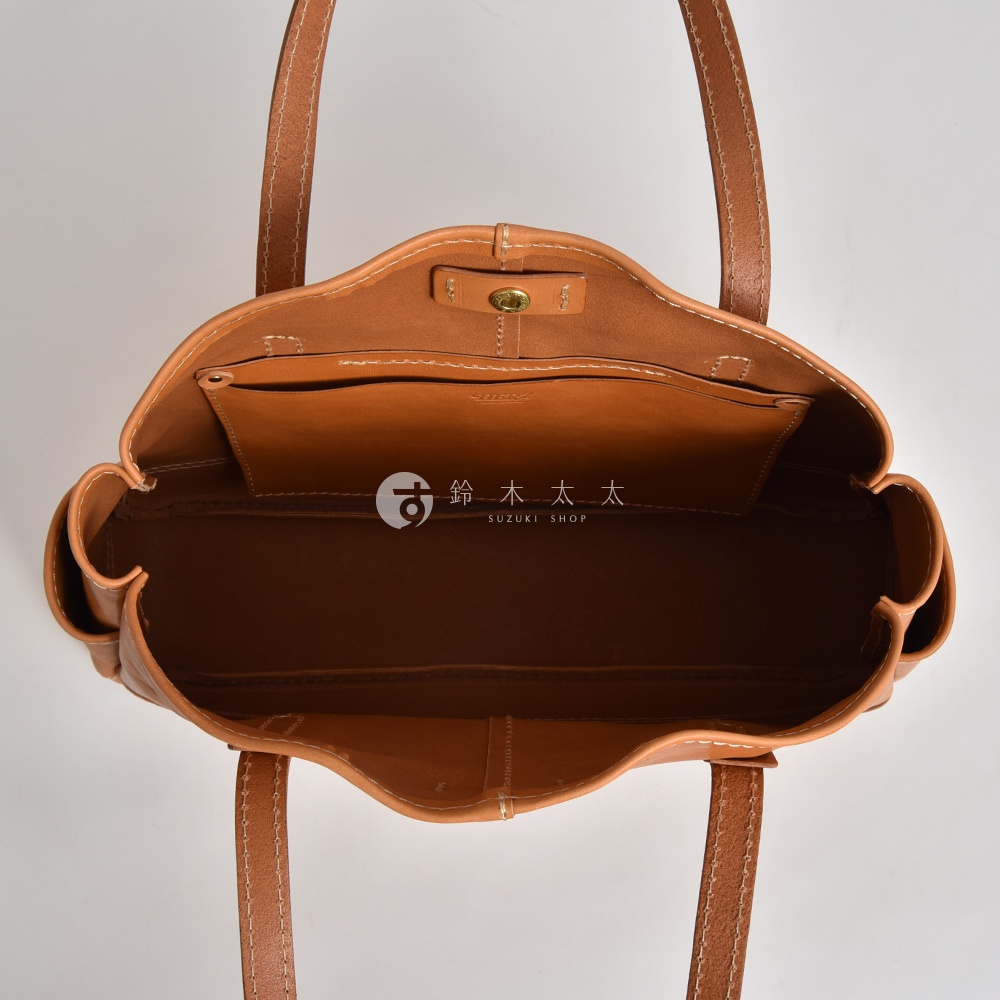從上方俯視的角度拍攝，展示了一款日本HERZ職人手作棕色皮革托特包的內部構造，包身為簡約的單層大空間設計，袋口設有金屬按扣，並印有SUZUKI SHOP品牌字樣，整體呈現出厚實溫潤的皮革質感與細膩的車縫工藝。