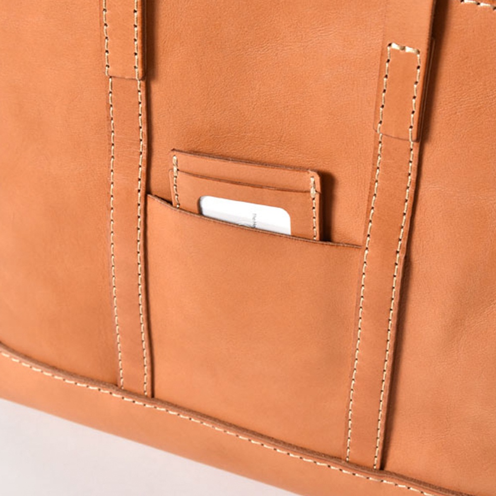 職人手作皮革經典托特包 T-9 M，採用天然棕色皮革，表面有精緻的縫線細節。包款設有外層口袋，可放入卡片或名片。