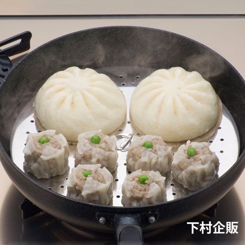 平底鍋內置不鏽鋼蒸盤，盛有兩個白色饅頭和六個頂部帶青豆的燒賣，蒸氣繚繞。
