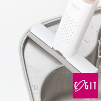 白色推拉式海綿清潔刷，帶有多孔設計，置於不鏽鋼水槽邊緣，水槽表面有水珠。