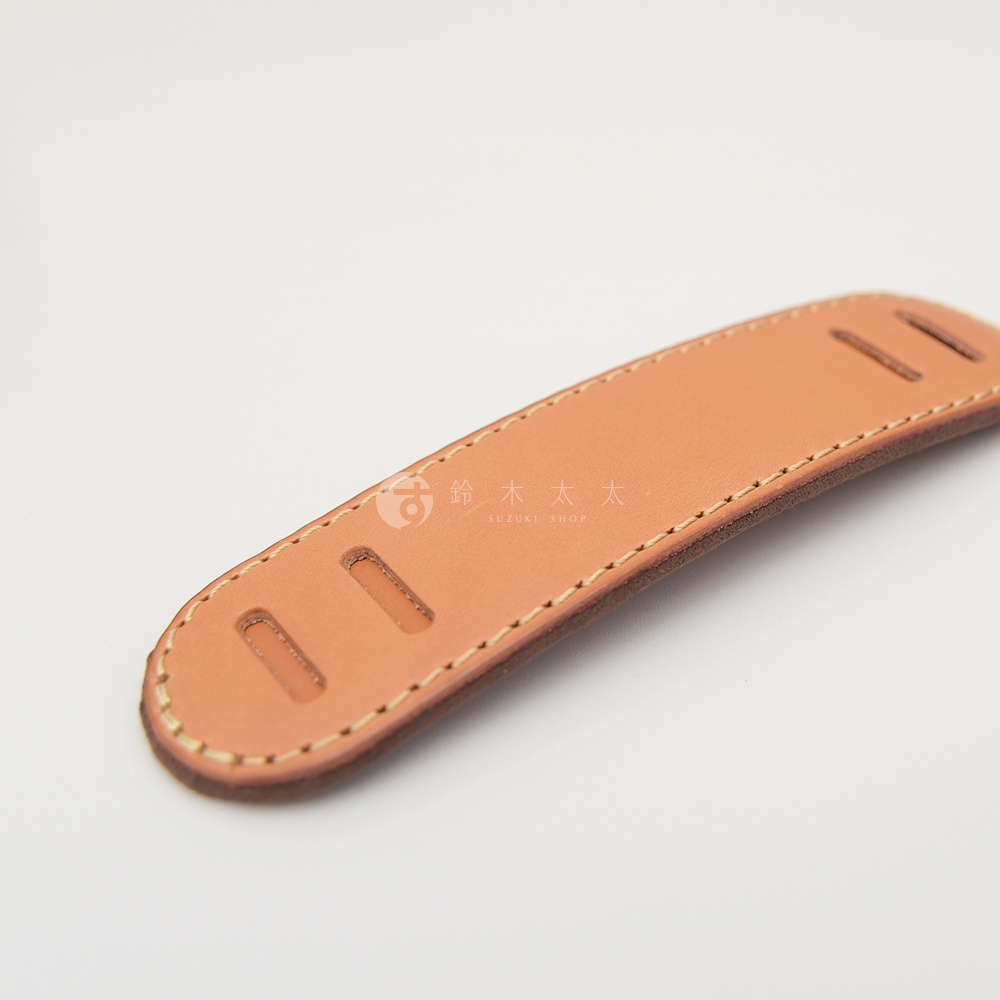 一塊淺棕色皮革製成的肩墊，帶有縫線和兩個用於固定或調整的長方形切口。