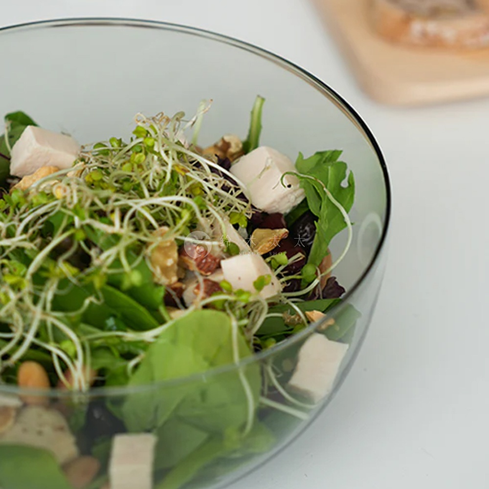 透明玻璃製成的圓潤點心碗，裝有豐富的沙拉，包含綠葉蔬菜、豆芽、堅果、雞肉塊和乾果。