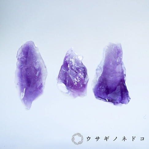 三塊紫水晶原石，呈現不規則的切面與深淺不一的紫色調，部分區域帶有晶體紋理。
