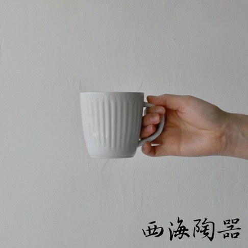 手持一個灰白色、帶有垂直紋路的陶瓷馬克杯，杯身呈圓柱形，有單個提把。