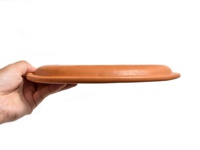 手持棕色皮革製成的職人手作圓形坐墊，展示其圓潤的邊緣及精細的縫線，材質呈現光滑質感。