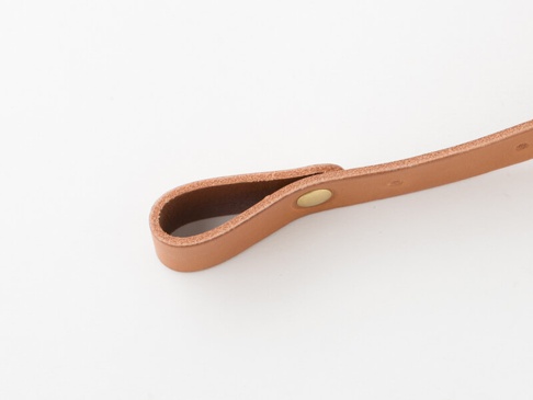 職人手作寬 3 公分的淺棕色皮革背包胸前扣帶，一端為皮革環扣，以黃銅色金屬釘固定。