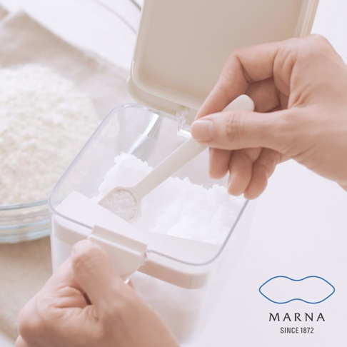 雙手正操作著MARNA密封防潮調味料盒，手部抓握容器邊緣並使用隨附的白色平口量匙舀取內容物，展示產品設計與便捷的使用體驗，右下方標註有MARNA SINCE 1872品牌字樣。