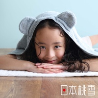 一個小女孩戴著一條有可愛熊耳朵的灰色連帽毛巾，她臉部朝鏡頭，雙手疊放在胸前，背景是淺藍色的牆壁。圖片右下角有「日本桃雪」的文字標誌。