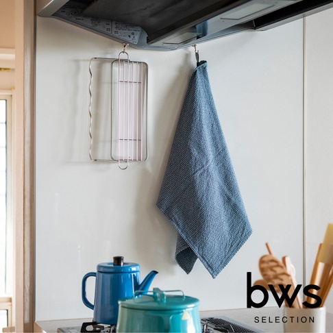 不鏽鋼折疊杯壺瀝水架，簡約銀色金屬材質，掛在廚房牆壁上，旁邊掛著藍色格紋抹布，下方擺放著藍色與綠色的茶壺。